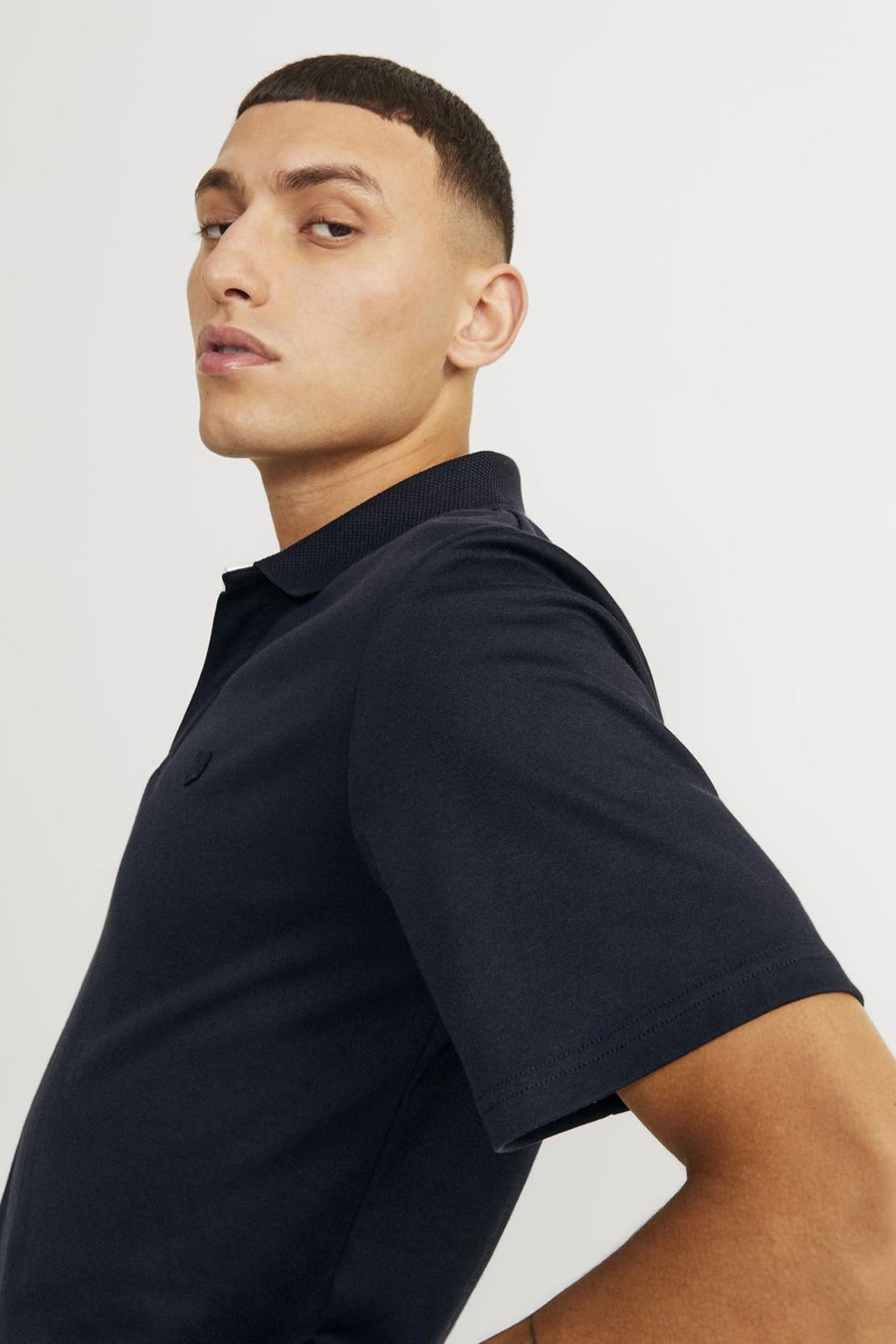 Blauw poloshirt van PREMIUM by JACK & JONES, van getextureerd katoen, gedragen door een man die zijdelings poseert.