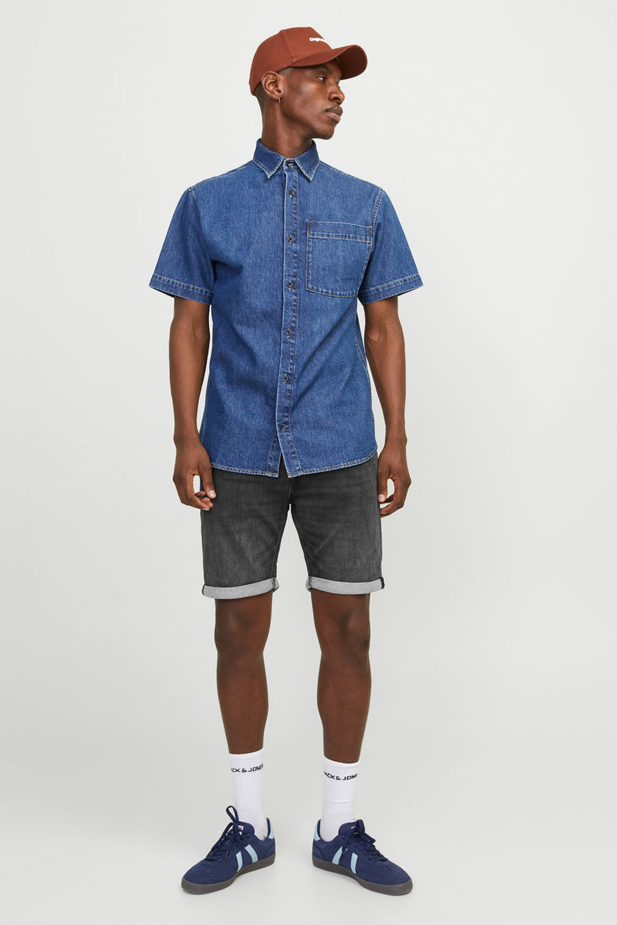 Korte zwarte denim broek van JACK & JONES JEANS INTELLIGENCE, met opgerolde zomen, gedragen met een spijkeroverhemd en sportschoenen.