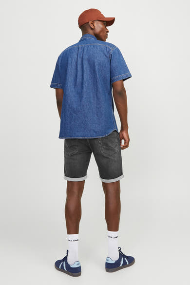 Korte zwarte denim van JACK & JONES JEANS INTELLIGENCE met omgeslagen zoom, gedragen met een overhemd en sneakers.