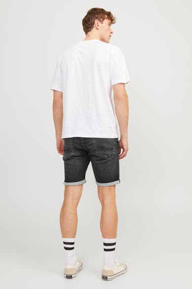 Korte zwarte spijkerbroek van JACK & JONES JEANS INTELLIGENCE, gedragen met een wit T-shirt en gestreepte sokken.