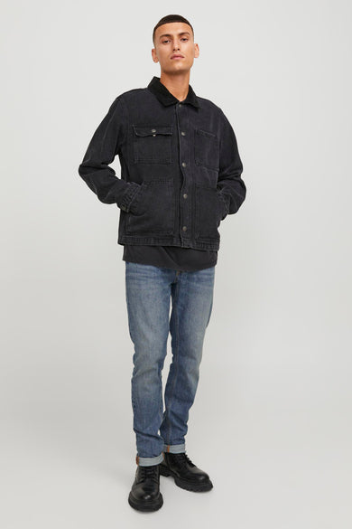Jean slim bleu moyen de JACK & JONES JEANS INTELLIGENCE, porté avec une veste en denim noire et des bottes en cuir noires.

