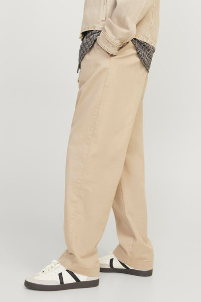 Ecru broek van JACK & JONES JEANS INTELLIGENCE, wijde pasvorm, gedragen met een geruit overhemd en witte sneakers met zwarte strepen.