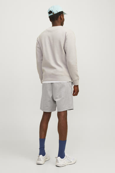 Korte grijze broek van JACK & JONES JEANS INTELLIGENCE gedragen met een sweatshirt, een T-shirt, een pet en sneakers.