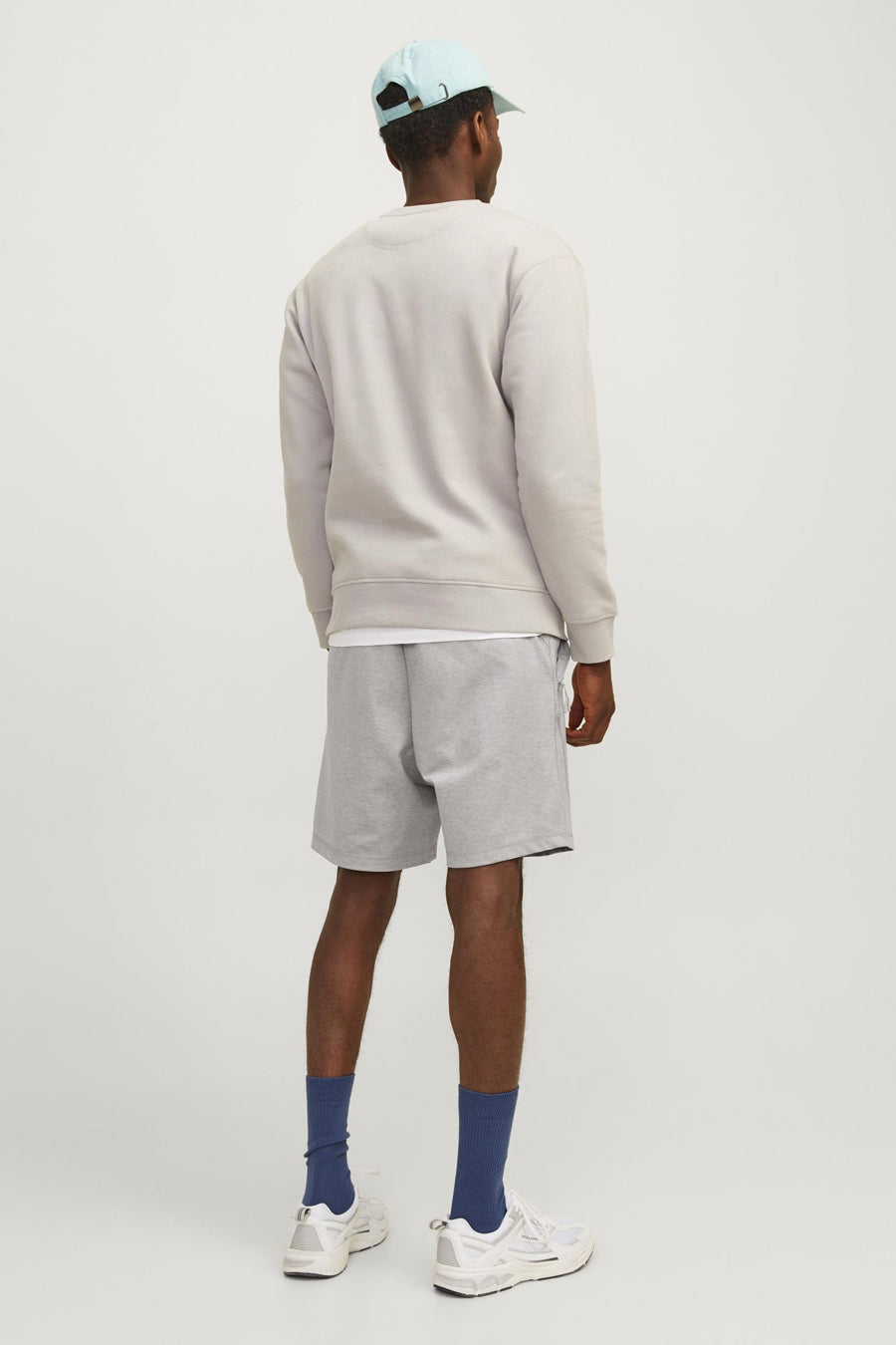 Korte grijze broek van JACK & JONES JEANS INTELLIGENCE gedragen met een sweatshirt, een T-shirt, een pet en sneakers.