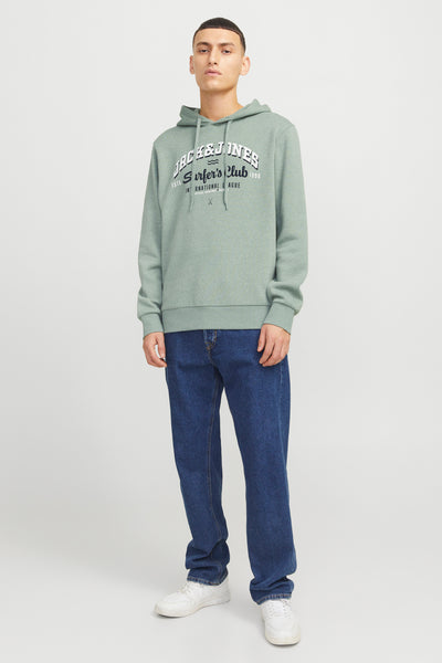 Sweat à capuche vert de ORIGINALS BY JACK & JONES, avec un imprimé graphique sur le devant, porté avec un jean bleu et des baskets blanches.
