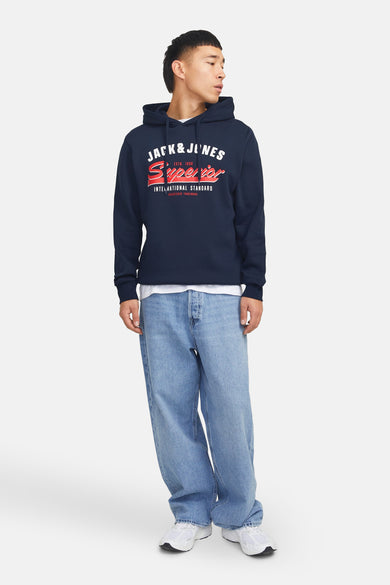 Sweat à capuche bleu marine de ORIGINALS BY JACK & JONES, avec un imprimé graphique et porté avec un jean ample et des baskets blanches.
