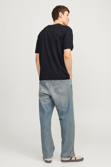 Zwart T-shirt met korte mouwen van JACK & JONES, gedragen met een wijde blauwe jeans en sportschoenen.