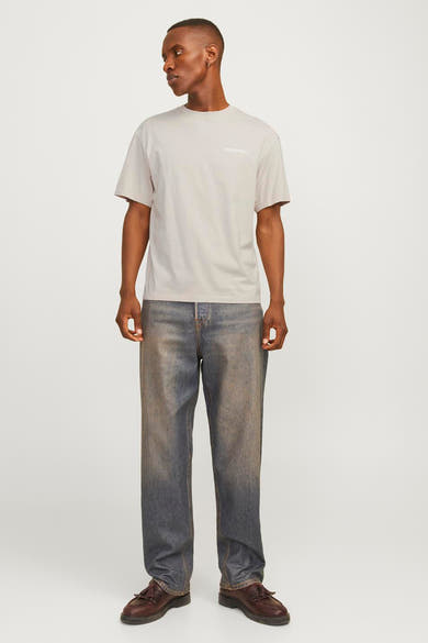 Beige T-shirt met korte mouwen van JACK & JONES, gedragen met een wijde, verbleekte spijkerbroek en bruine loafers.