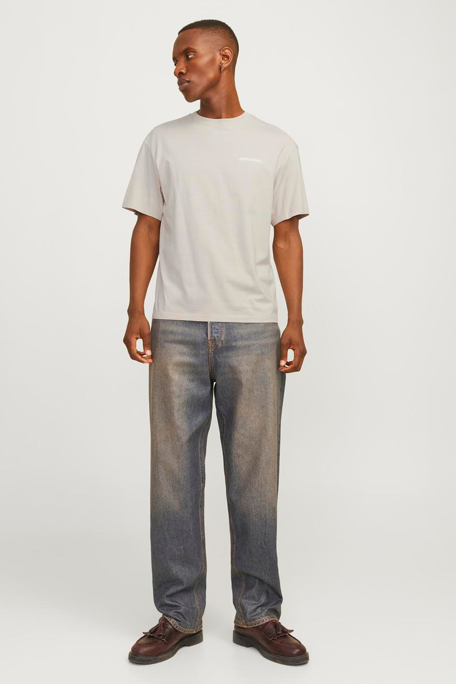 Beige T-shirt met korte mouwen van JACK & JONES, gedragen met een wijde, verbleekte spijkerbroek en bruine loafers.
