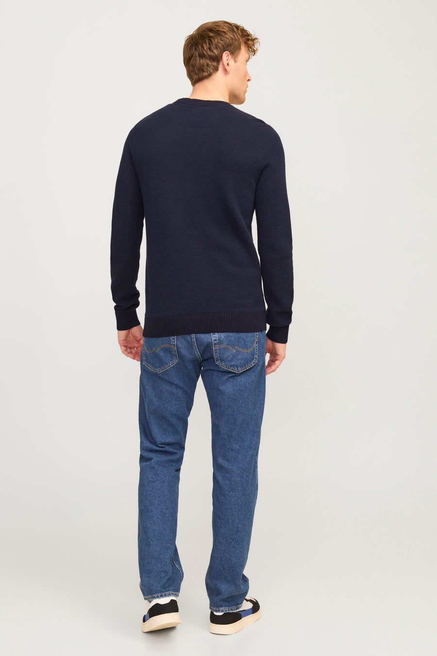 Pull à col rond bleu de JACK & JONES, avec une texture en maille gaufrée, porté avec un jean bleu et des baskets.