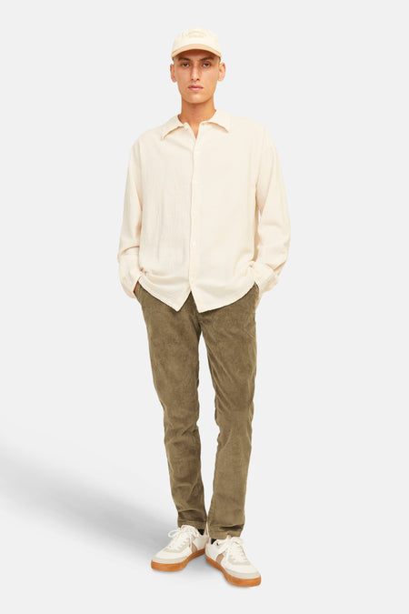 Bruin seizoensbroek van corduroy van JACK & JONES JEANS INTELLIGENCE, gedragen met een beige overhemd en een beige pet.