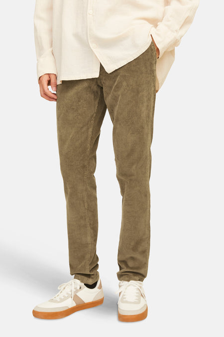 Bruine herfstbroek van ribfluweel van JACK & JONES JEANS INTELLIGENCE, gedragen met een beige overhemd en witte sneakers.