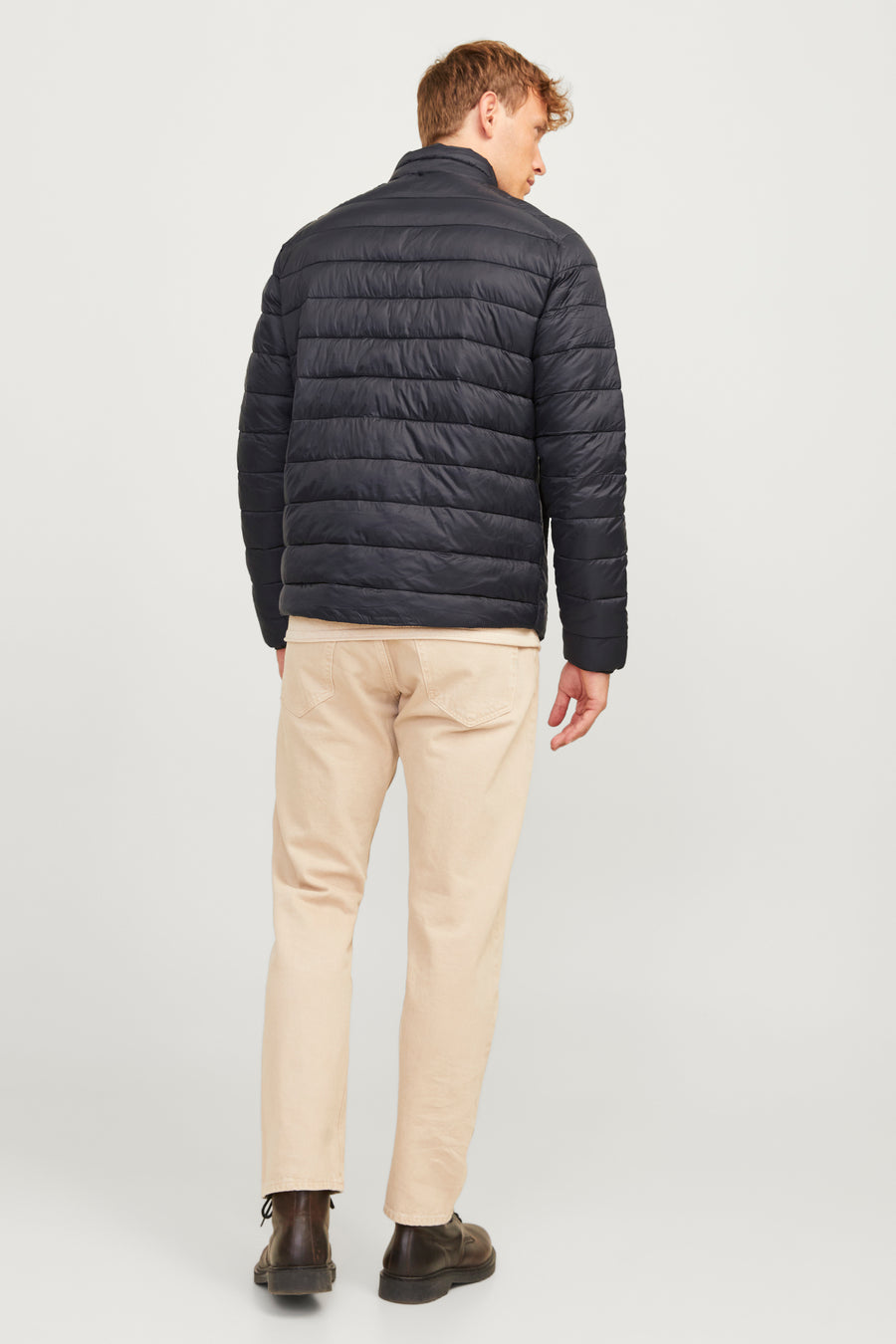 Korte zwarte jas, ORIGINALS BY JACK & JONES, gedragen met een beige broek en bruine laarzen, van achteren gezien.