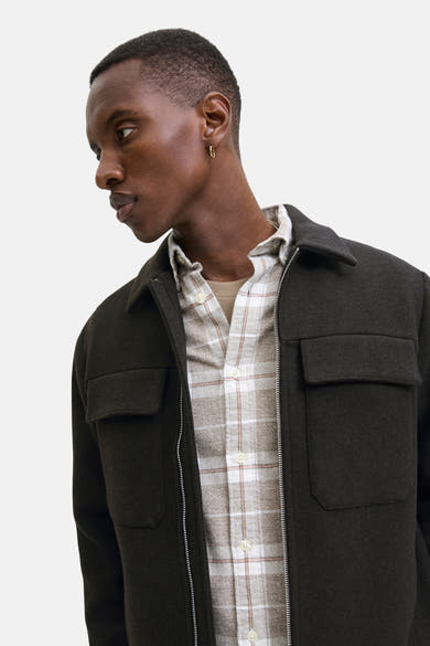 Kort bruin jack van PREMIUM by JACK & JONES, met rits en opgestikte zakken, gedragen over een geruit overhemd.