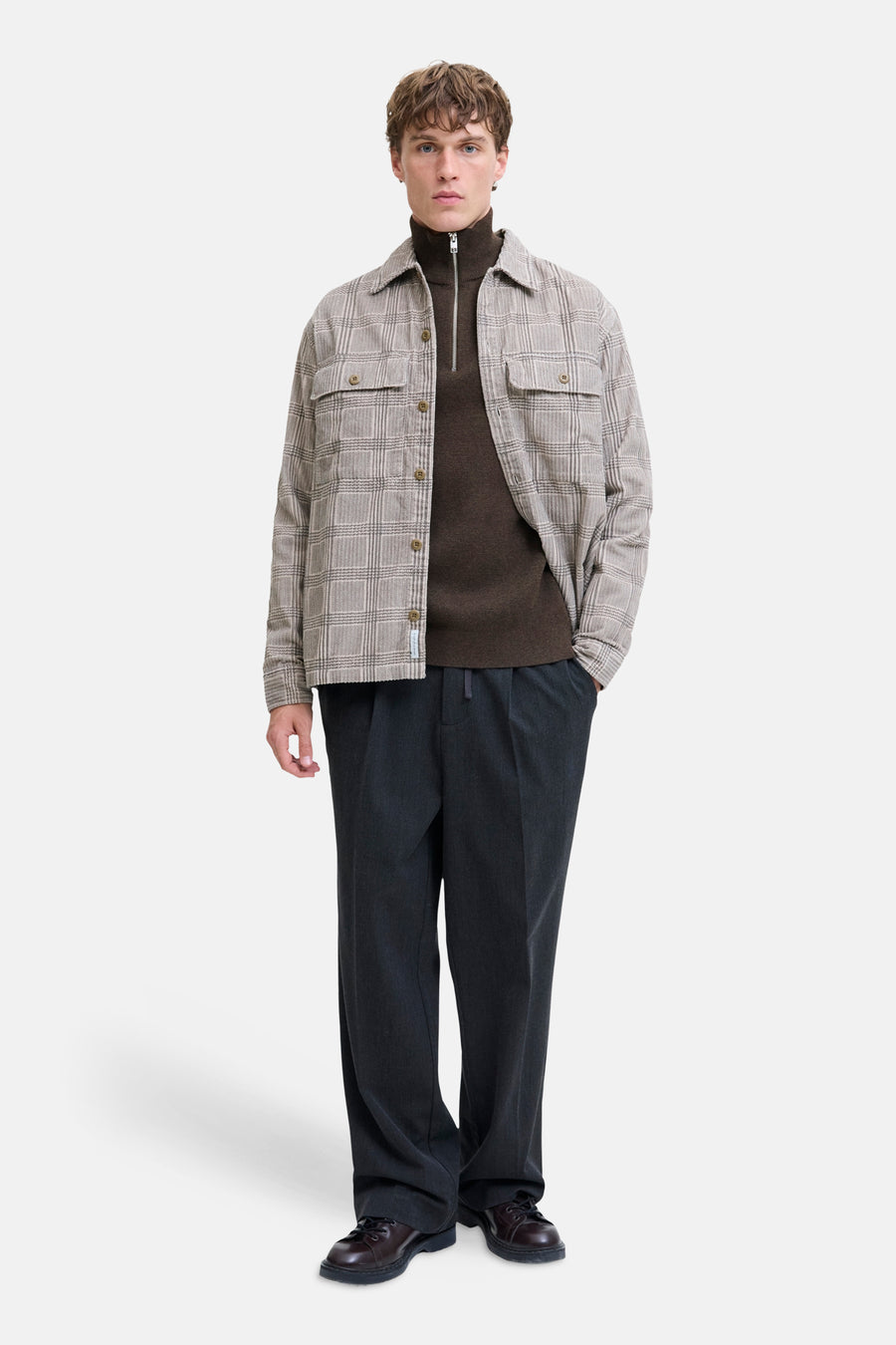 Brown ribbed turtleneck sweater with front zipper, worn under plaid shirt, paired with dark trousers and brown leather shoes, full-length front view.
