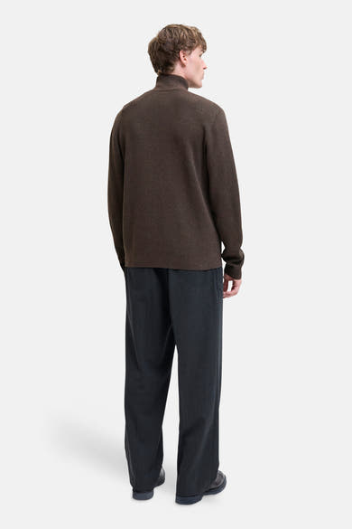 Brown turtleneck sweater by [brand omitted] shown from back, ribbed texture, long sleeves, paired with dark trousers and black shoes.