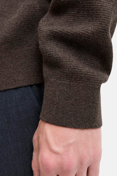 Brown ribbed knit turtleneck sweater close-up showing textured fabric and cuff detail on model's arm