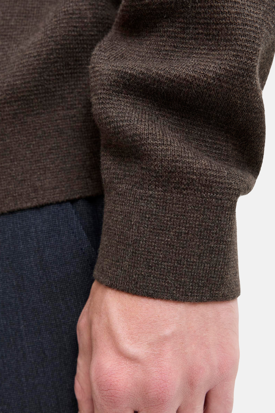 Brown ribbed knit turtleneck sweater close-up showing textured fabric and cuff detail on model's arm