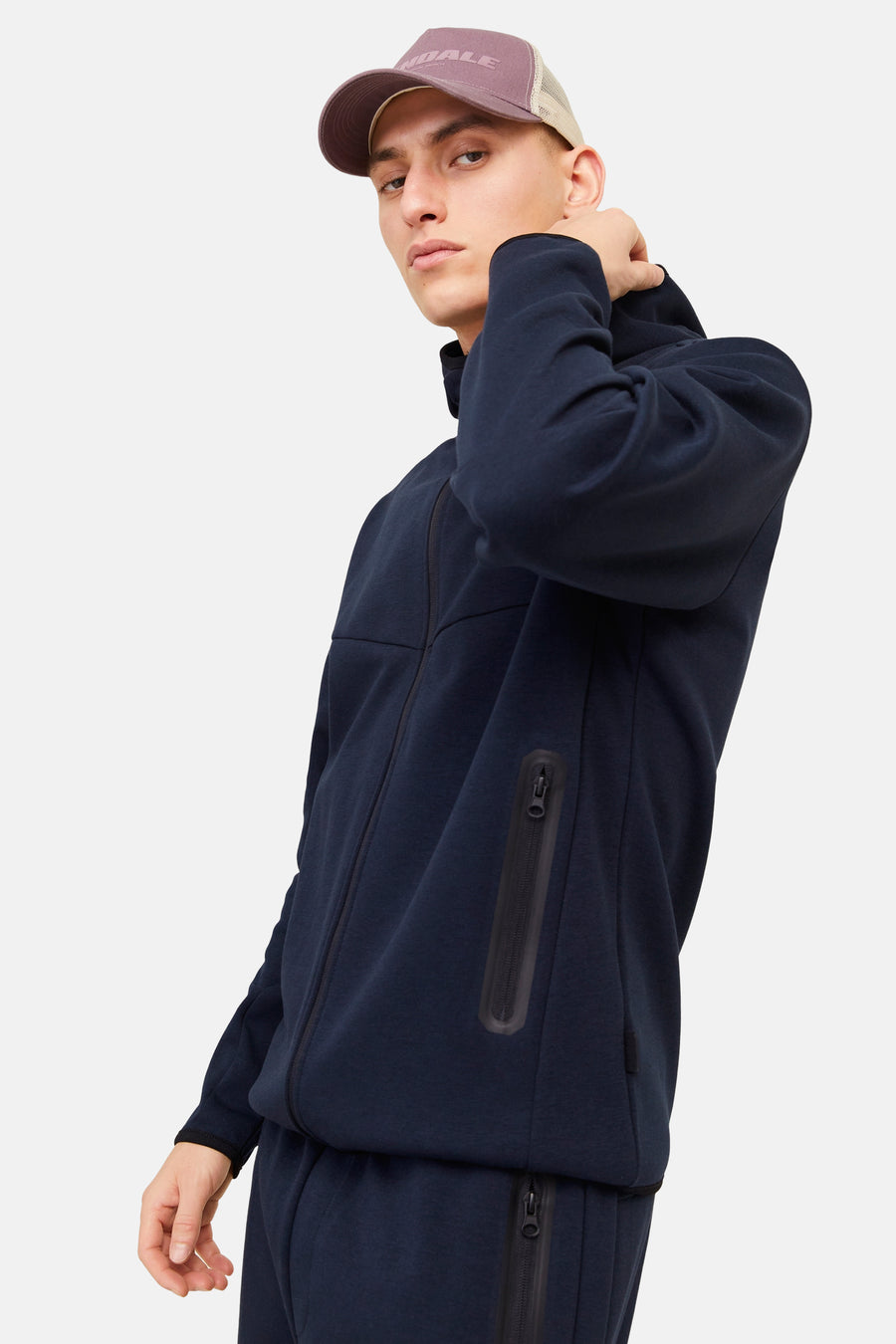 Donkerblauwe bodywarmer van JACK & JONES, met capuchon en ritssluiting, gedragen met een bruine pet.