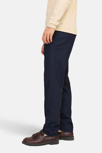 Pantalon de costume bleu par JACK & JONES JEANS INTELLIGENCE, porté avec un pull beige et des mocassins marron, vue de côté.
