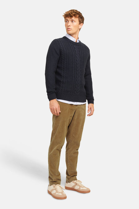 Pantalon de costume beige en velours côtelé par JACK & JONES, porté avec un pull marine à torsades et des baskets claires, vue de profil.