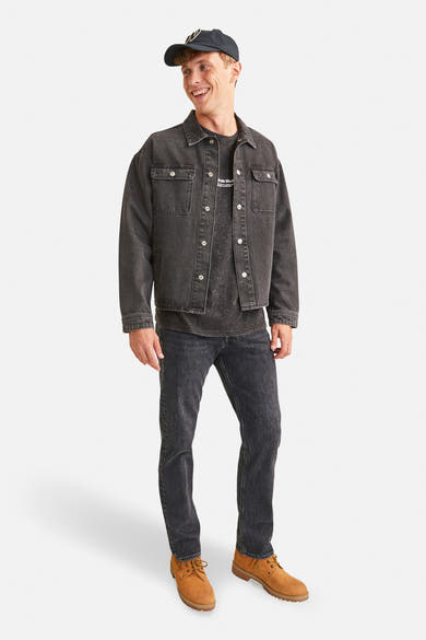 Zwarte tapered jeans van JACK & JONES JEANS INTELLIGENCE, gedragen met een zwarte spijkerjas en bruine schoenen.