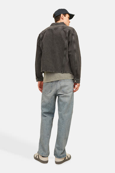 Wijde spijkerbroek in lichtblauw denim van JACK & JONES JEANS INTELLIGENCE, gedragen met een zwart jasje en beige schoenen.