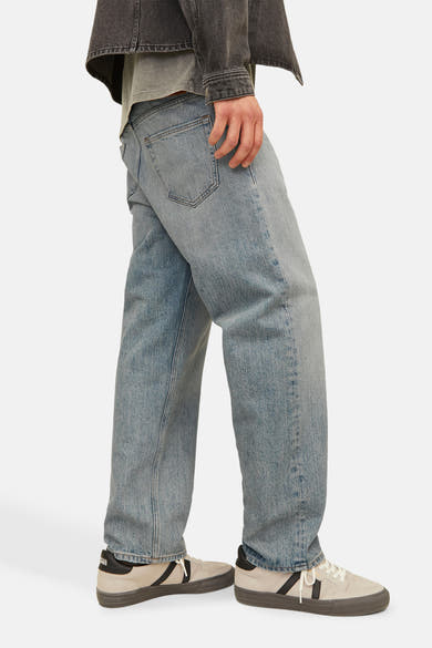 Wijde spijkerbroek in lichtblauw denim van JACK & JONES, gedragen met een grijs jasje en sneakers.