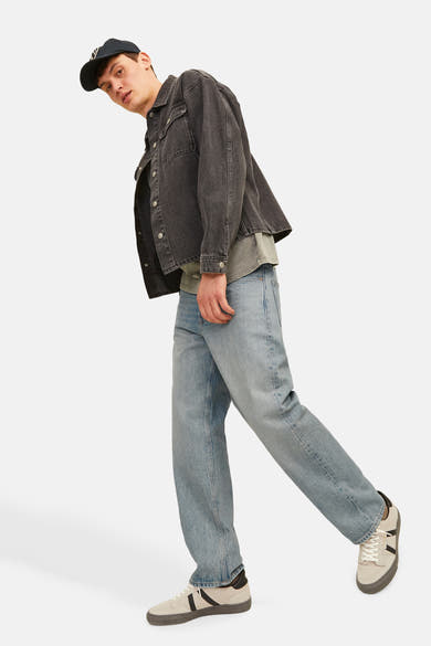 Wijde spijkerbroek in lichtblauw denim van JACK & JONES JEANS INTELLIGENCE, gedragen met een zwarte spijkerjas en beige sneakers.