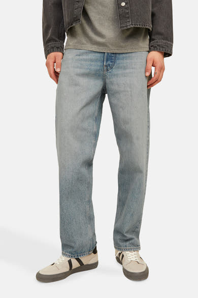 Wijde spijkerbroek in lichtblauw denim van JACK & JONES, gedragen met een grijs T-shirt en een zwarte jas.