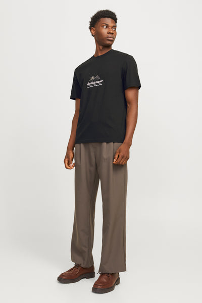 T-shirt à manches courtes noir de JACK & JONES, avec un imprimé graphique montagneux, porté avec un pantalon taupe et des chaussures marron.
