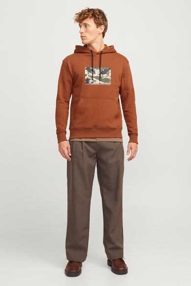 Sweat à capuche marron by ORIGINALS BY JACK & JONES, avec motif graphique sur le devant, porté avec un pantalon et des chaussures marron.
