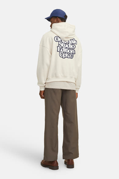 Gebroken wit hoodie van ORIGINALS BY JACK & JONES, met opdruk op de rug, gedragen met een bruine broek en schoenen.