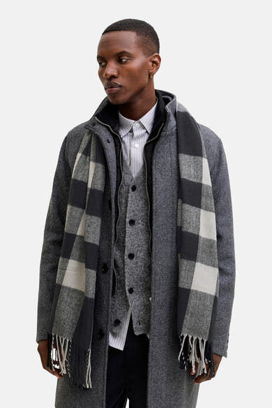 Écharpe noire par ACCESSORIES BY JACK & JONES, motif à carreaux gris, à franges, portée avec manteau et veste assortis.
