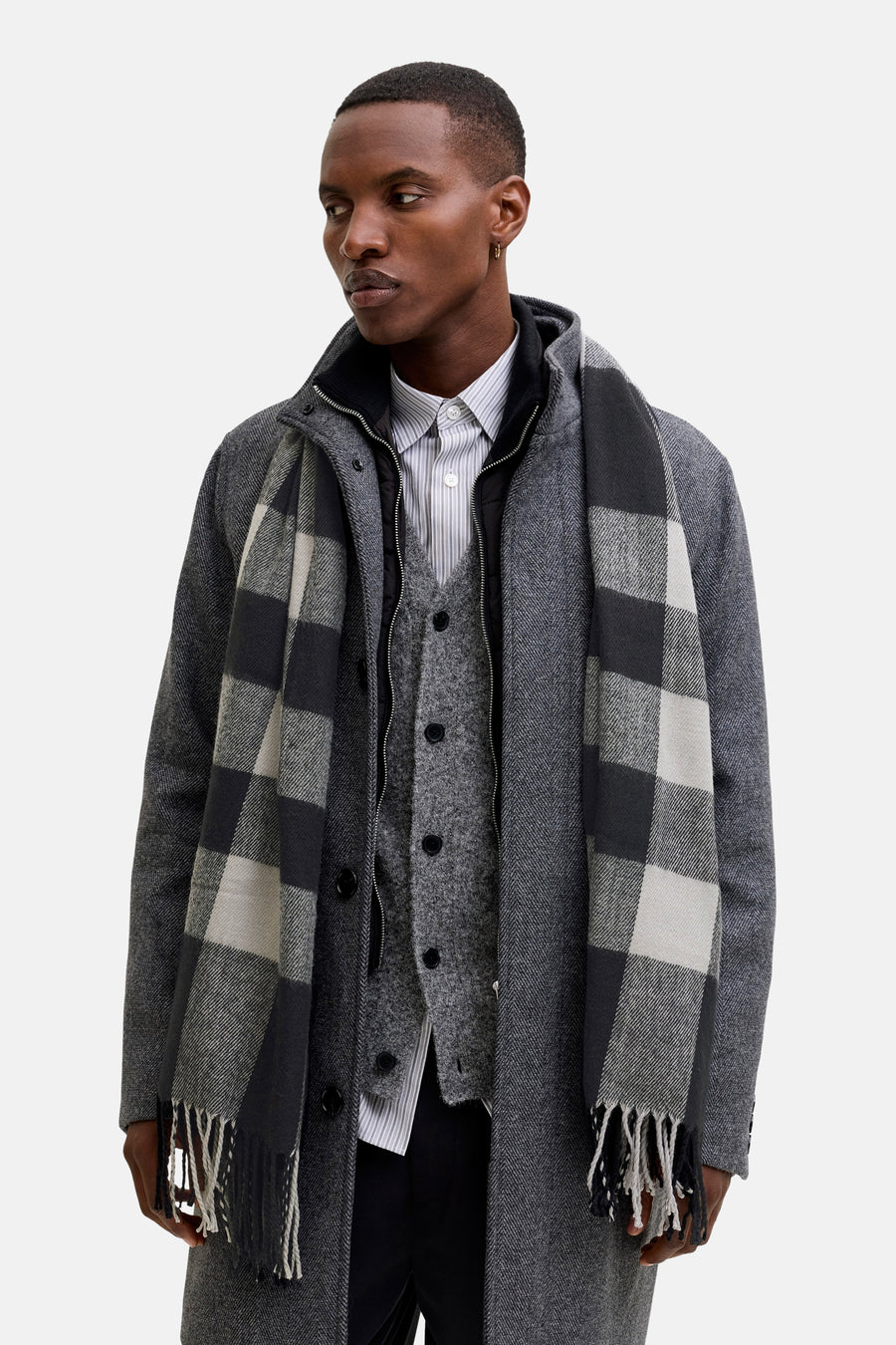 Écharpe noire par ACCESSORIES BY JACK & JONES, motif à carreaux gris, à franges, portée avec manteau et veste assortis.
