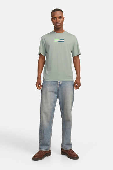 T-shirt à manches courtes vert, de JACK & JONES, avec logo graphique sur la poitrine, porté avec un jean ample bleu.