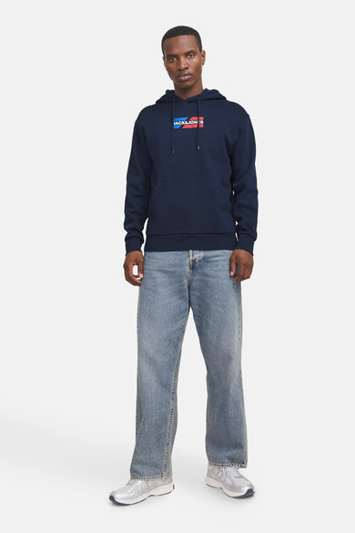 Marineblauwe hoodie van JACK & JONES, met een rechthoekig logo op de borst, gedragen met een wijde jeans en zilveren sneakers.
