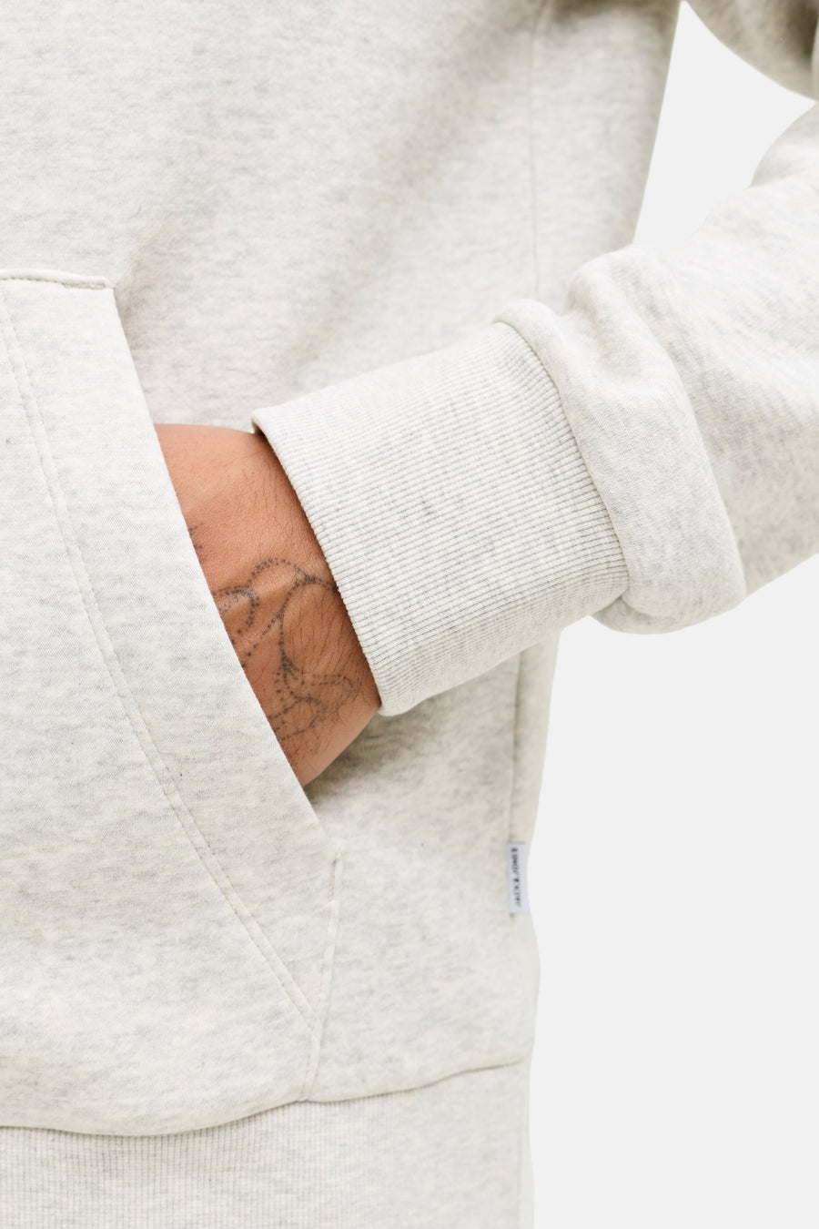 Ecru hoodie van JACK & JONES, met een kangoeroezak en geribbelde manchetten, gedragen met een zichtbare tatoeage.