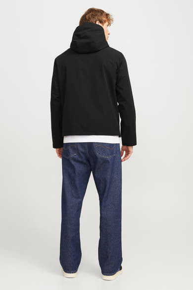 Veste courte noire de JACK & JONES, avec capuche, portée sur un t-shirt blanc et un jean bleu ample.
