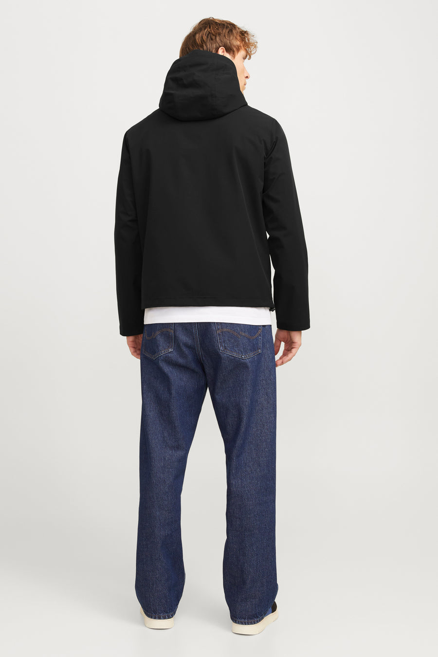 Veste courte noire de JACK & JONES, avec capuche, portée sur un t-shirt blanc et un jean bleu ample.