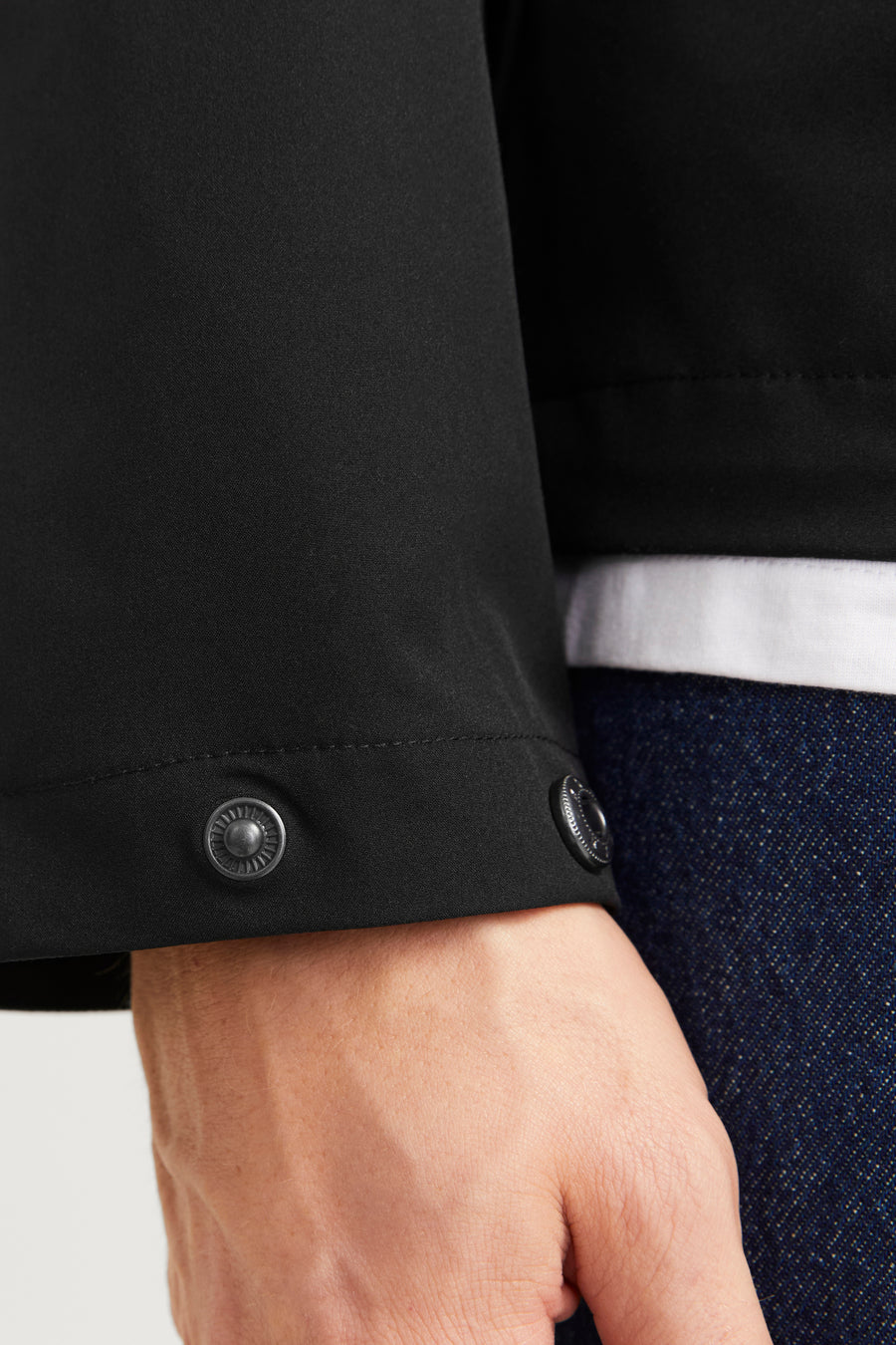 Veste courte noire de JACK & JONES avec boutons-pression métalliques sur la manche, portée avec un t-shirt blanc et un jean bleu.