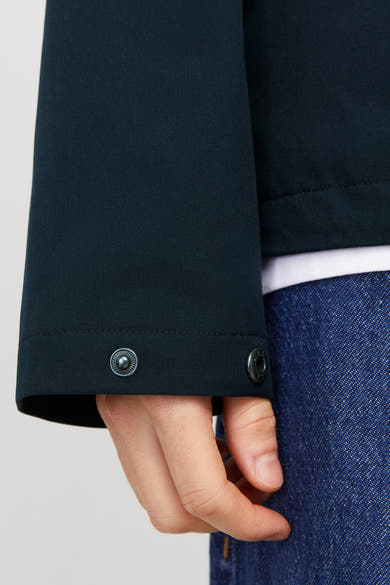 Kort blauw jack van JACK & JONES, met metalen drukknoppen op de manchetten, gedragen over een wit T-shirt en een spijkerbroek.