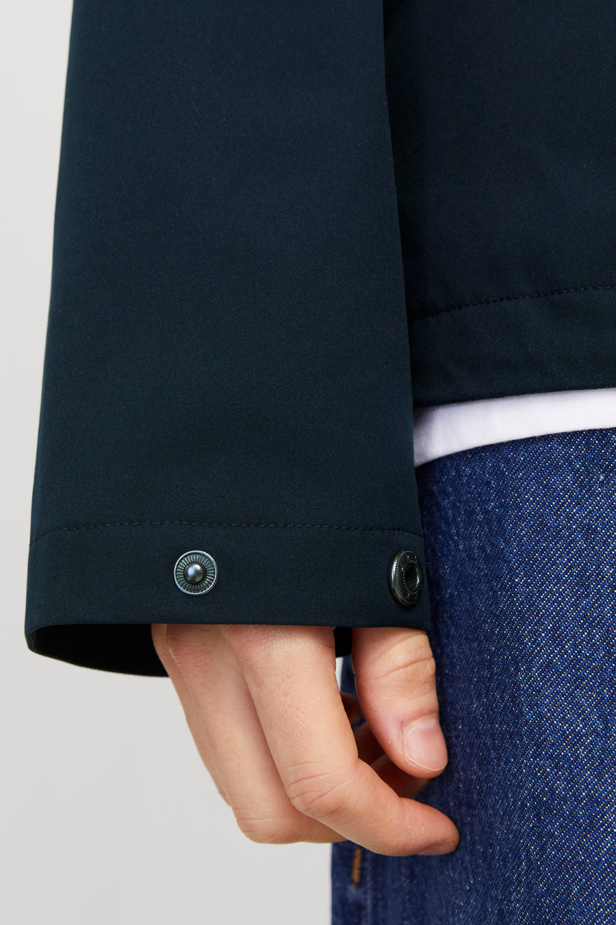 Kort blauw jack van JACK & JONES, met metalen drukknoppen op de manchetten, gedragen over een wit T-shirt en een spijkerbroek.