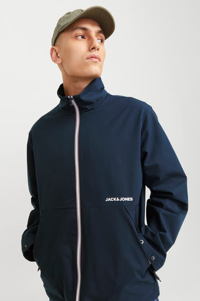 Korte blauwe jas van JACK & JONES, met witte ritssluiting en rode strepen, gedragen met een groene pet.
