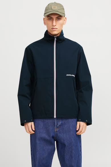 Korte blauwe jas van Jack & Jones, met witte ritssluiting en gedragen met een blauwe jeans.