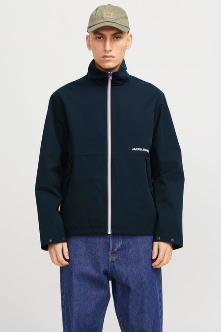 Korte blauwe jas van Jack & Jones, met witte ritssluiting en gedragen met een blauwe jeans.