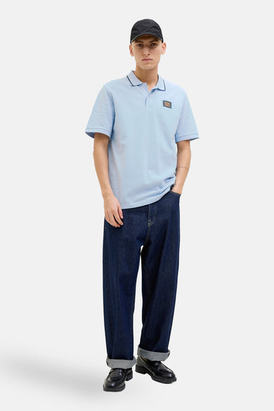 Polo bleu à manches courtes par JACK & JONES, porté avec un pantalon ample en denim foncé et des mocassins.