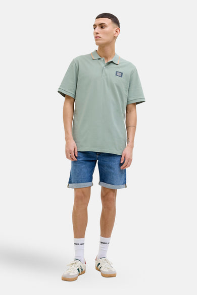 Polo kaki à manches courtes de JACK & JONES, avec col contrastant et logo sur la poitrine, porté avec un short en jean.
