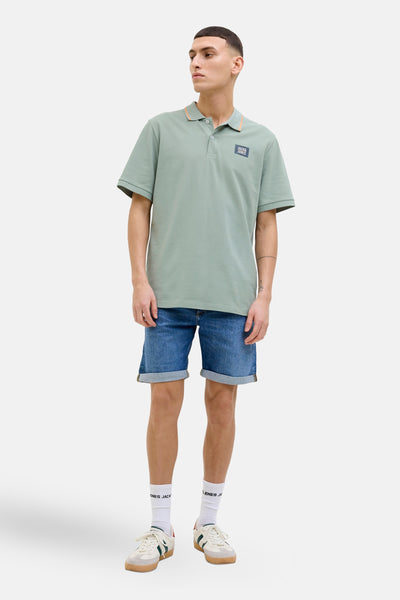 Polo kaki à manches courtes de JACK & JONES, avec col contrastant et logo sur la poitrine, porté avec un short en jean.
