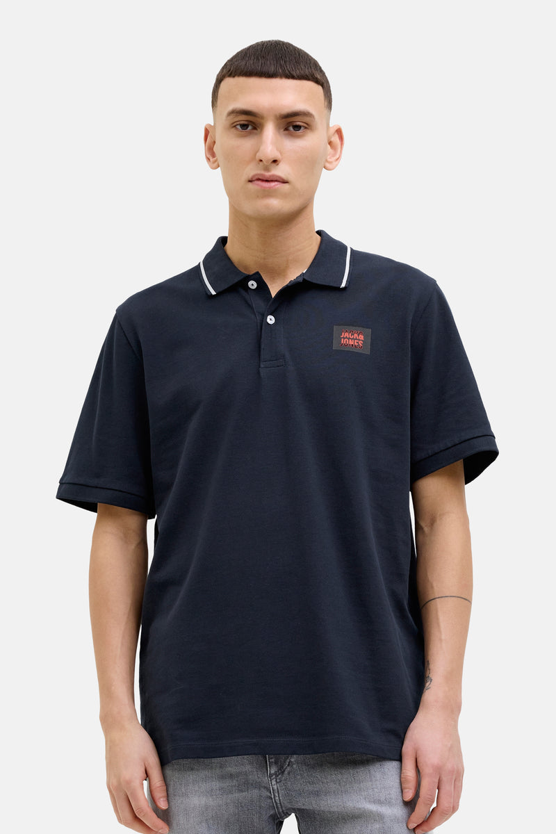 Donkerblauwe polo met korte mouwen van JACK & JONES, met vierkant logo op de borst, gedragen met een spijkerbroekshort.